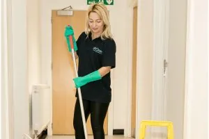 Office cleaner mopping corridor floor with wet floor sign in place 