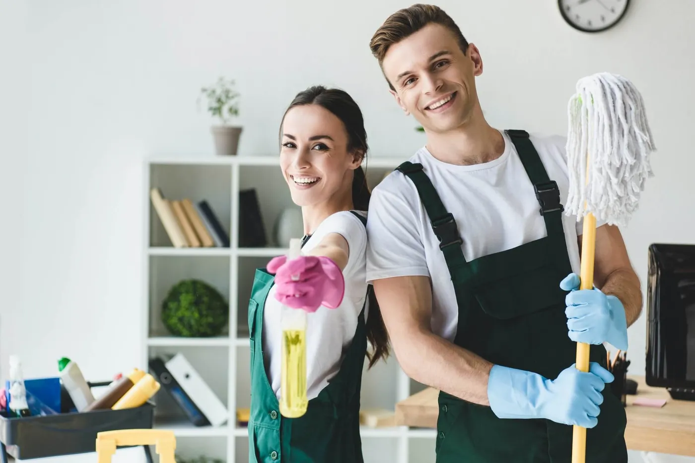 Happy young cleaners with mop and spray bottle smiling at camera while cleaning office in Horsham