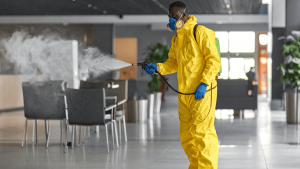 Technician in yellow hazmat suit using fogging equipment to disinfect a commercial interior
