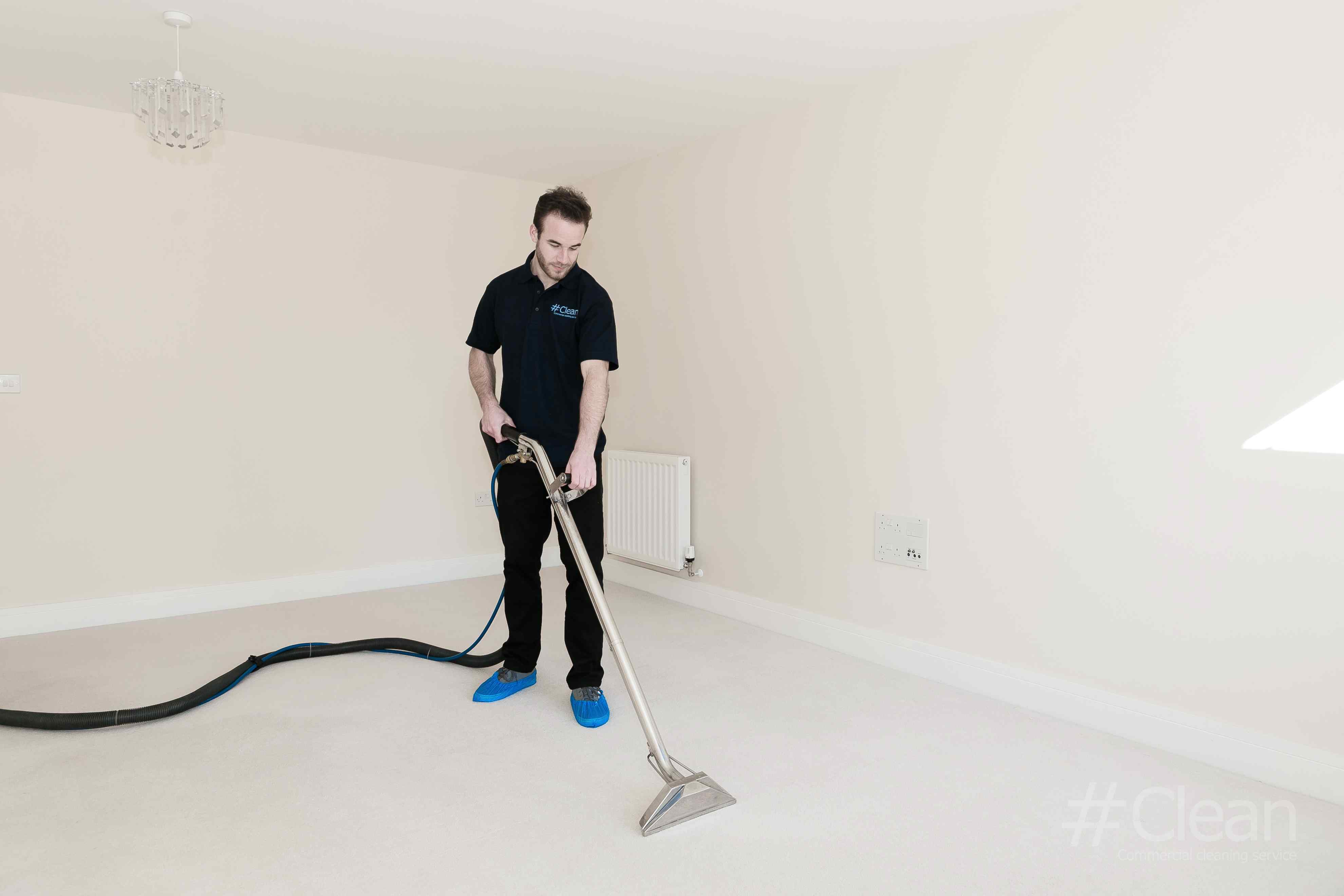 Man In Hashtag Clean Uniform Hoovering A Room