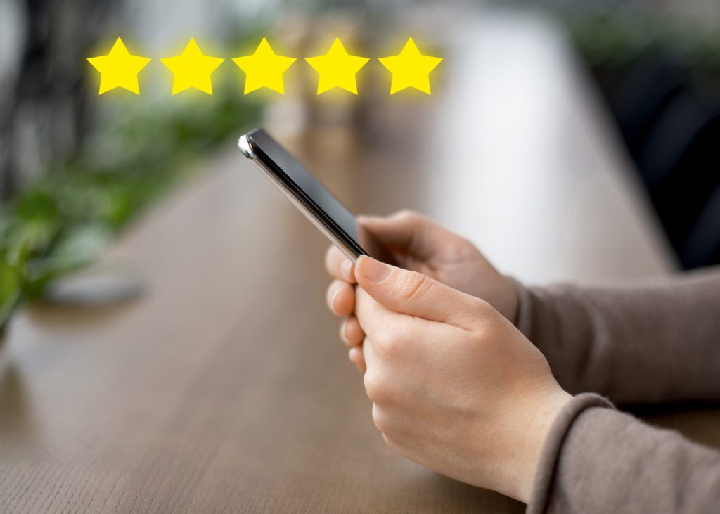 Close-up of a person holding a smartphone with five yellow stars above, symbolising a positive customer review or five-star service rating.