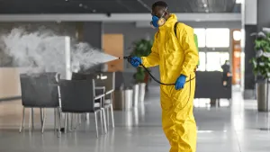 Technician in yellow hazmat suit using fogging equipment to disinfect a commercial interior