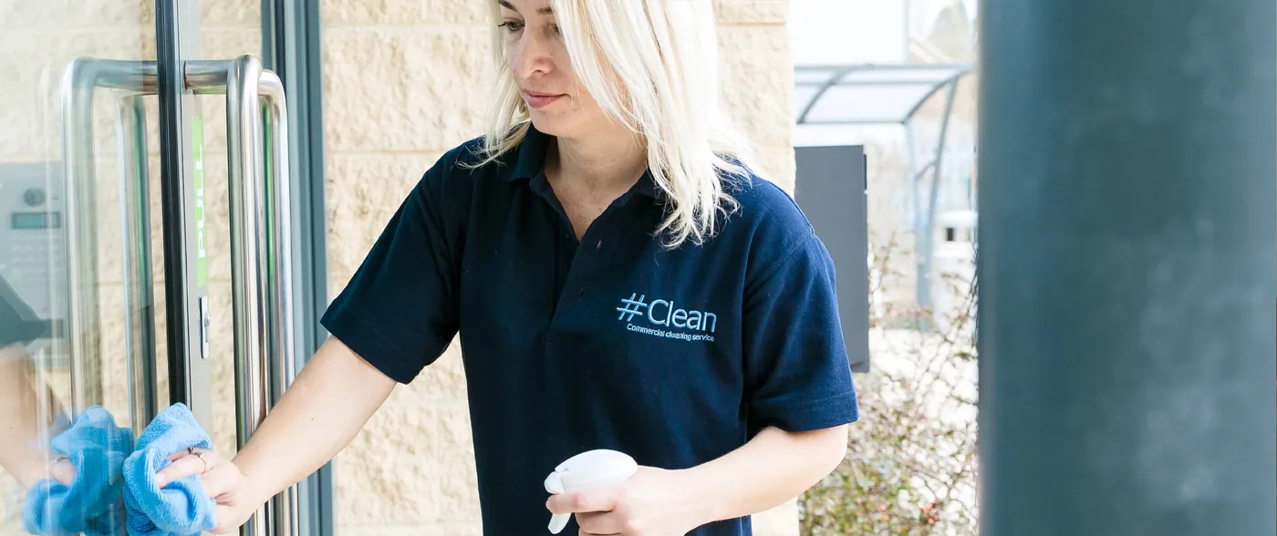 Cleaner carrying out professional office cleaning by sanitising glass doors