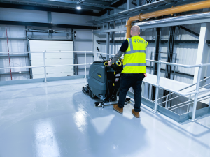 Operative carrying out a commercial deep clean of an industrial floor using a ride-on scrubber dryer
