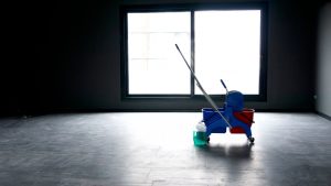 A professional cleaning trolley with a mop, blue and red buckets, and a green spray bottle sitting in an empty room ready for an end of tenancy clean.