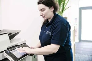 A Hashtag Clean staff member wiping down the screen of a printer or copier with a white cloth, ensuring all surfaces are sanitized.