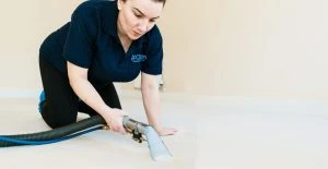 A staff member from Hashtag Clean in a blue polo shirt deep cleaning a light-coloured carpet.